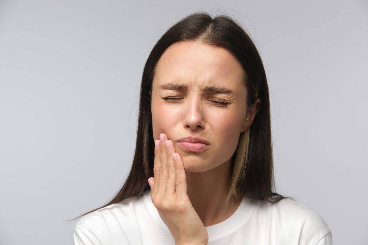 Toothache concept. Studio shot of young female feeling pain, holding her cheek with hand, suffering from bad tooth ache